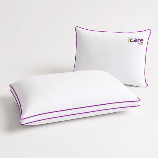 Two white icare Cloud Pillows with purple piping, with the front pillow showing the 'icare pillows' logo on the back, set against a clean white background.