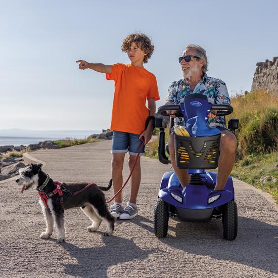 Man on a Invacare Leo Mobility Scooter with a young boy and a dog by the seaside.