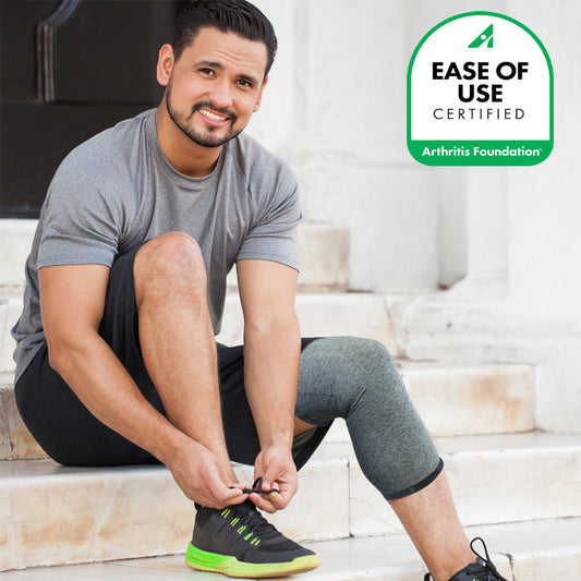 Man sitting on steps with an IMAK Compression Arthritis Knee Sleeve tying his shoe with 'Ease of Use Certified' Arthritis Foundation logo.