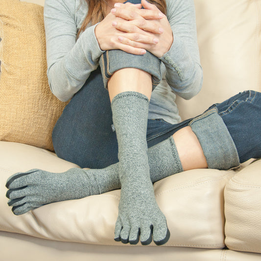 Person wearing IMAK Compression Arthritis Socks sitting on a couch.