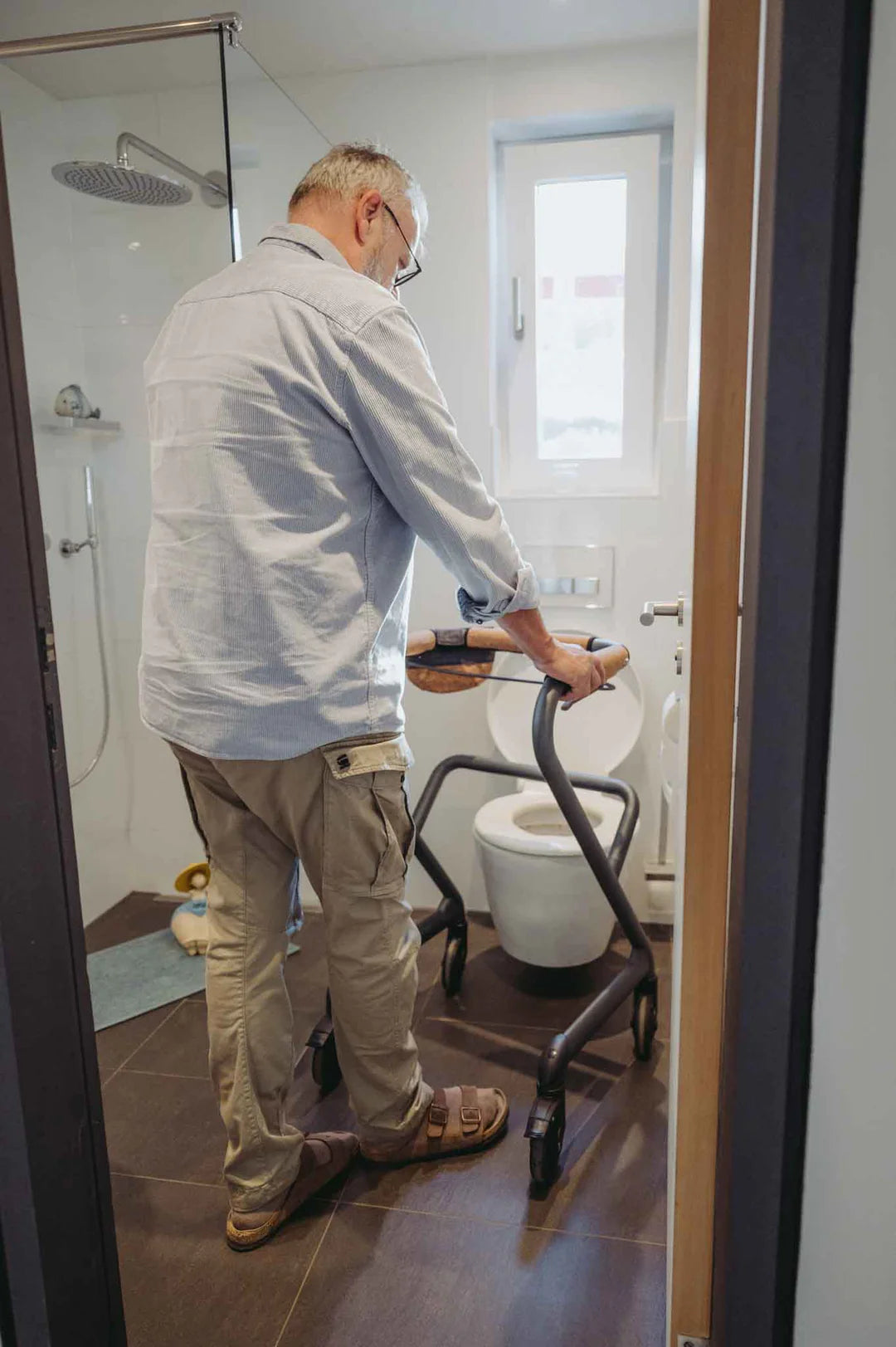Person using a Saljol Indoor Walker in a bathroom with a toilet and shower.