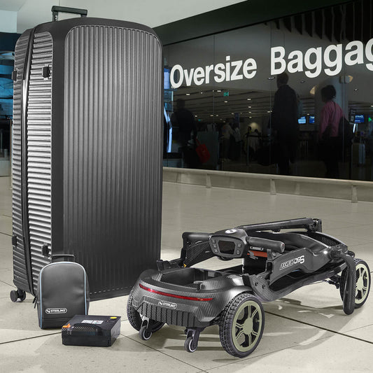 A large black ribbed hard-shell suitcase stands next to a STERLING S50 Carbon Folding Mobility Scooter and matching small bag in an airport terminal. A glass sign in the background reads 'Oversize Baggage'.