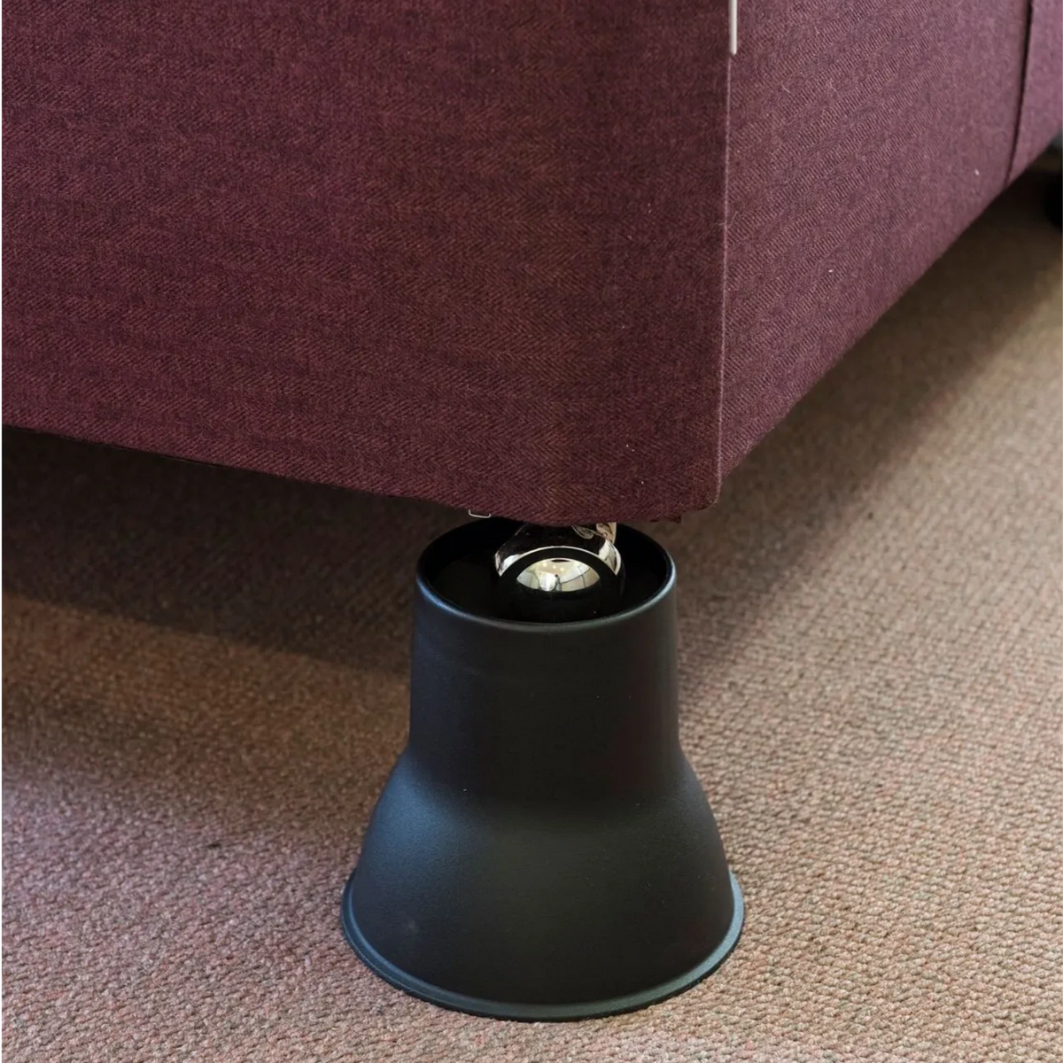 A close-up of a Derby Elephant Feet Furniture Raiser 14cm the corner of a burgundy upholstered bed, placed on a textured beige carpet.