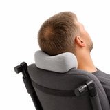 A man reclining in a dark gray chair with his head resting on a light gray icare Reform Neck Support pillow, shown from the back against a white background.
