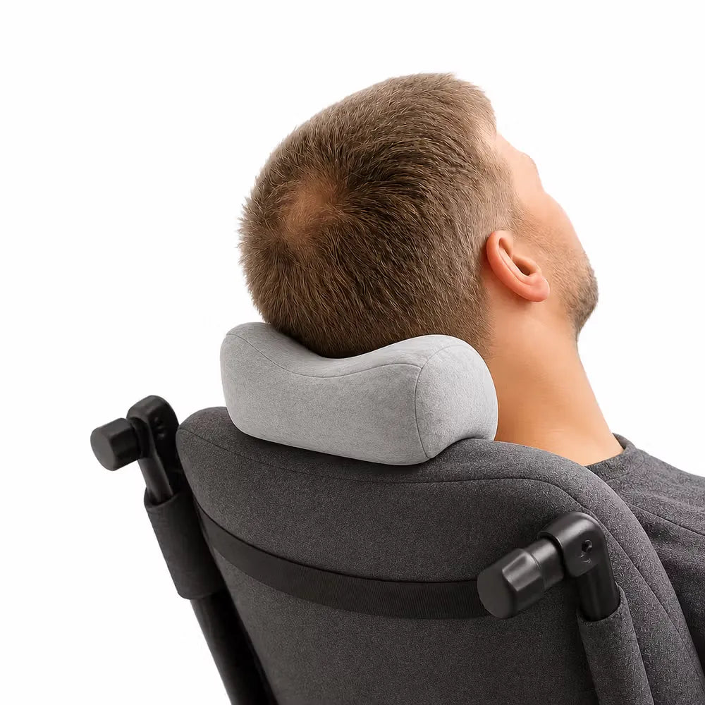 A man reclining in a dark gray chair with his head resting on a light gray icare Reform Neck Support pillow, shown from the back against a white background.