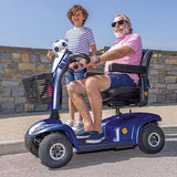 Man and child on an Invacare Leo Mobility Scooter with a stone wall and clear sky background