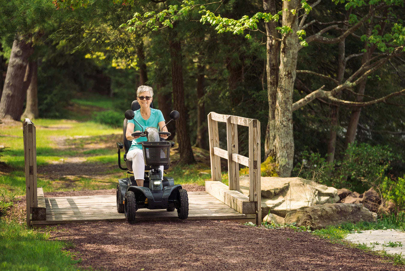 Person using a Pride Mobility Pathrider Endurance Mobility Scooter Black on a wooden ramp in a park setting