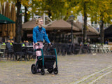 Person pushing a Rollz Motion Performance 2-in-1 Walker Wheelchair in an outdoor setting with trees and tables in the background