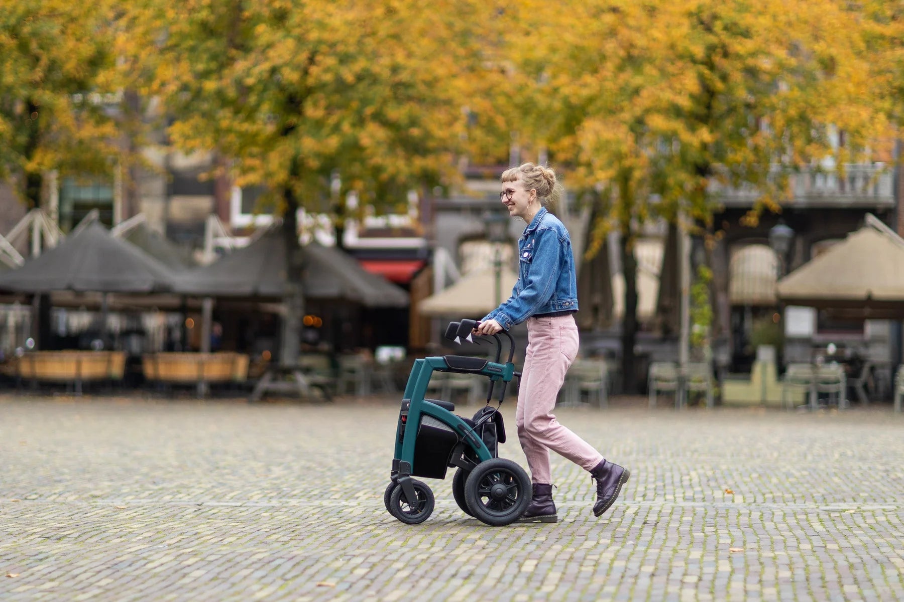 Person using a Rollz Motion Performance 2-in-1 Walker Wheelchair in an outdoor setting with trees and buildings in the background