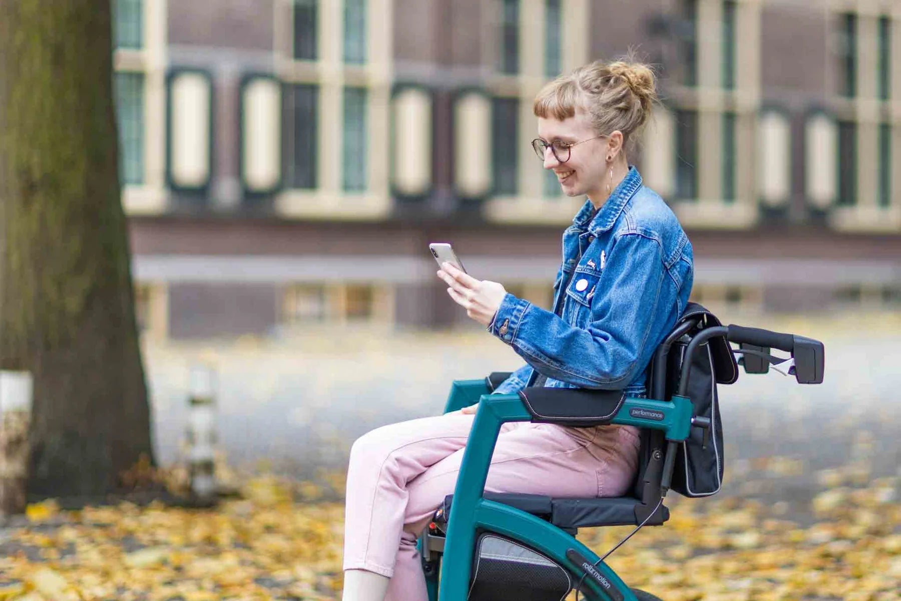 Person using a smartphone while sitting in a Rollz Motion Performance 2-in-1 Walker Wheelchair outdoors.