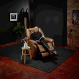 Woman sitting in a Theorem Mercer Power Lift Recliner Chair Saddle reading a book in a dimly lit room with a brick wall.