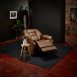 Theorem Mercer Power Lift Recliner Chair Saddle in a dimly lit room with dark walls and a brick wall.