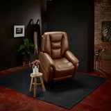 Theorem Mercer Power Lift Recliner Chair Saddle in a dimly lit room with a dark wall and brick wall.