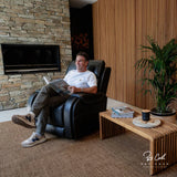 Man sitting in a Theorem Seagrove Power Lift Recliner Midnight Chair reading a magazine in a cozy living room.