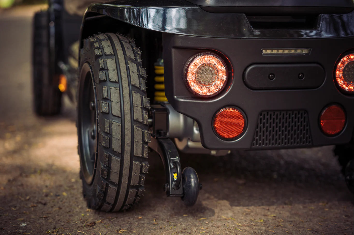 Close-up of a Pride Mobility Pathrider Endurance Mobility Scooter Black rear wheel and lights on a road.