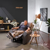 Man relaxing in aMan standing next to a Theorem Studio Power Lift Recliner Chair in Fog in a modern living room.