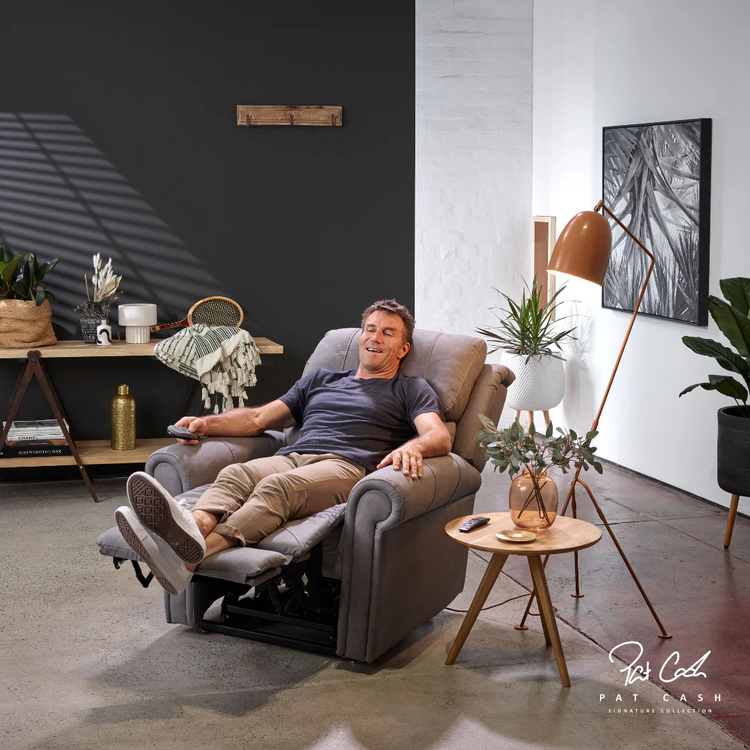 Man relaxing in aMan standing next to a Theorem Studio Power Lift Recliner Chair in Fog in a modern living room.