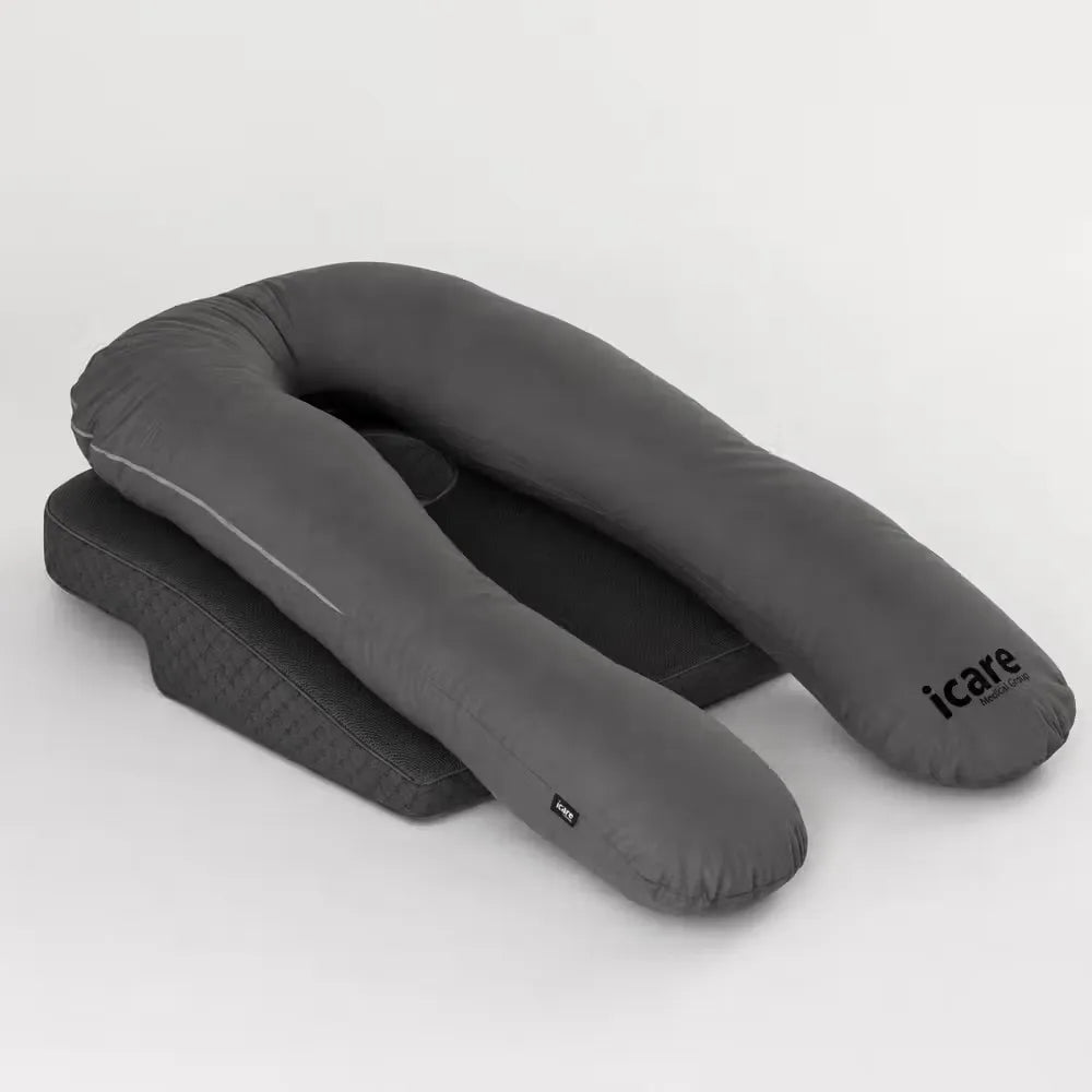 A dark gray U-shaped icare body pillow pregnancy support pillow with a matching icare Supporta Rotator Cuff Recovery Pillow underneath, shown on a light gray studio background. The brand name 'icare' is printed on the side of the U-pillow.