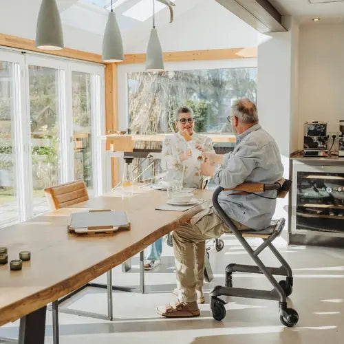 Two people sitting with Saljol Indoor Walker at a table in a modern kitchen with large windows.