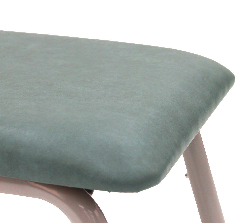 Close-up of a padded upholstered surface in a muted sage green color, showing part of the rounded corner and a light pink metal support leg against a white background.