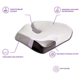 A contoured icare Reform Seat Support
 pillow with a white and dark gray design, surrounded by purple callout lines and text highlighting its ergonomic features, including a coccyx relief cutout, contoured thigh supports, and an anti-slip base.