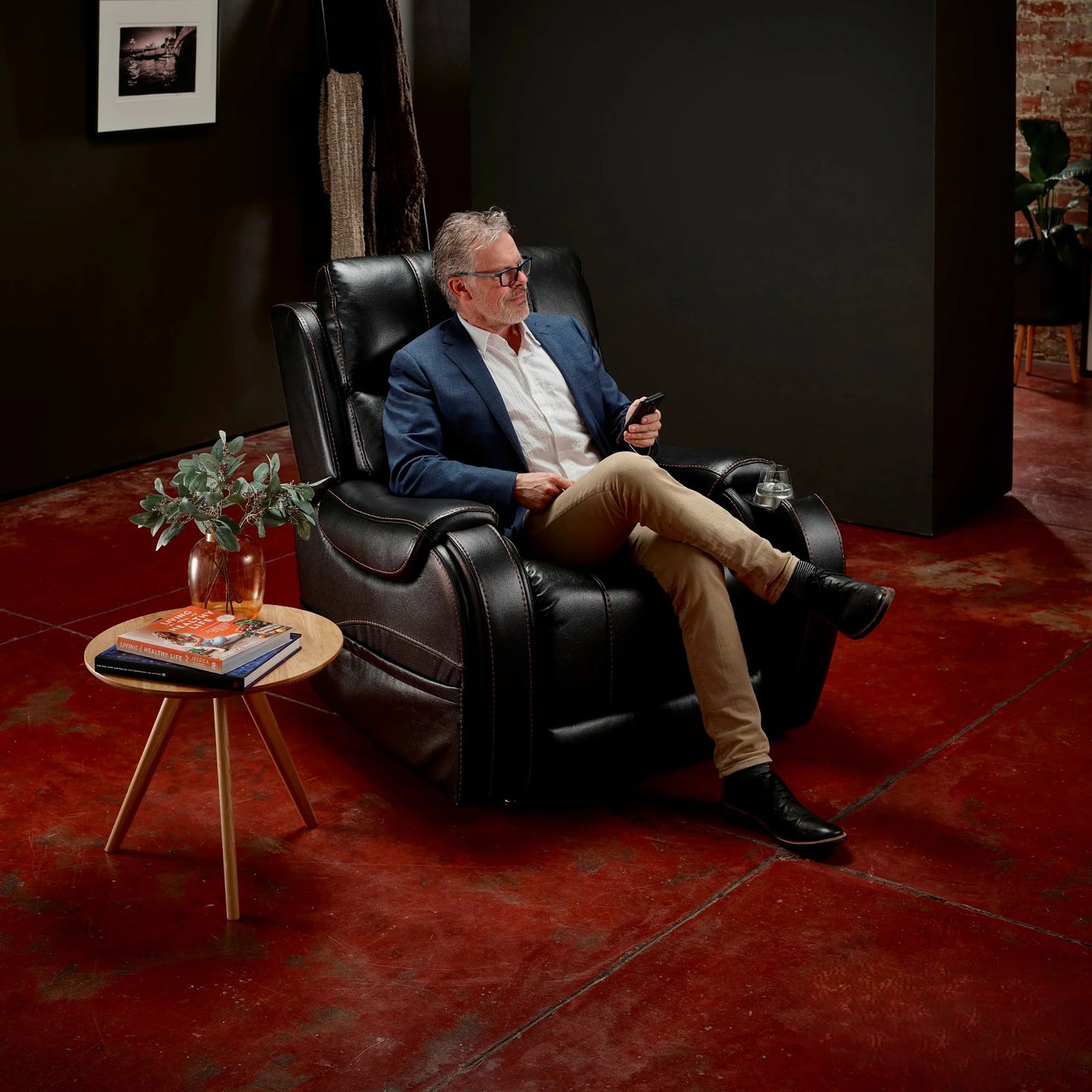 Man sitting in aMidnight Theorem Seagrove Power Lift Recliner Chair in a dimly lit room with a small table and plant.