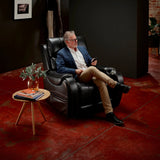 Man sitting in aMidnight Theorem Seagrove Power Lift Recliner Chair in a dimly lit room with a small table and plant.