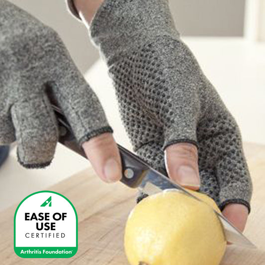 Person wearing IMAK Compression Active Gloves cutting a lemon with a knife on a wooden surface, featuring the Arthritis Foundation ease of use certification logo.