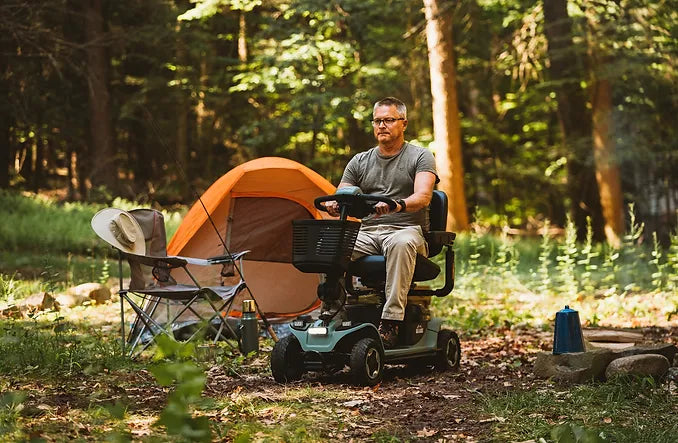 Man using a Pride Mobility Baja Bandit Mobility Scooter near an orange tent in a forest setting