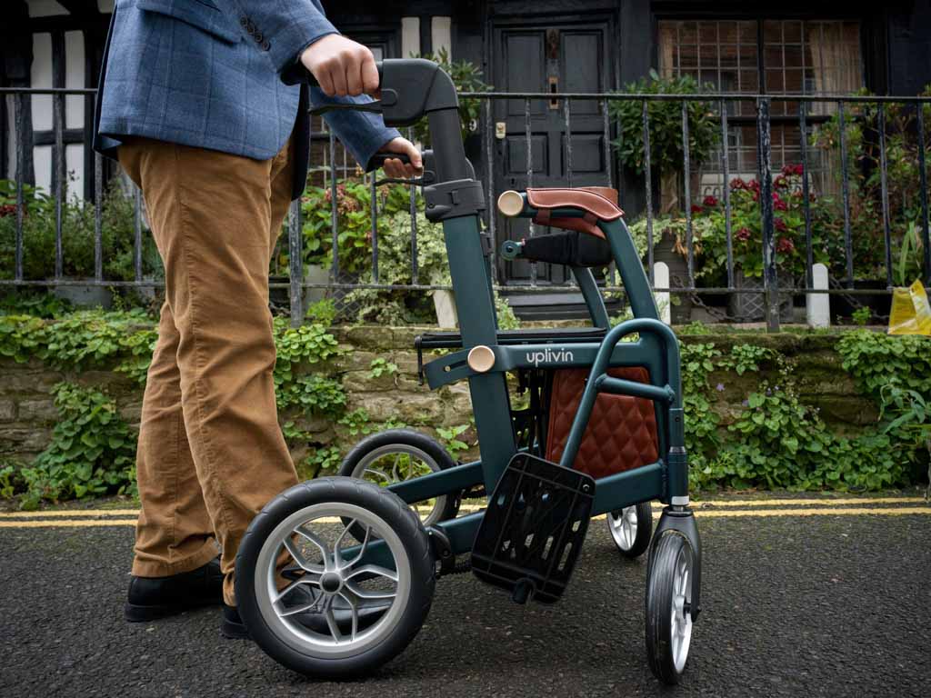 Person pushing a greenUplivin Gavo 2-in-1 Walker Wheelchair with a brown seat in an outdoor setting.