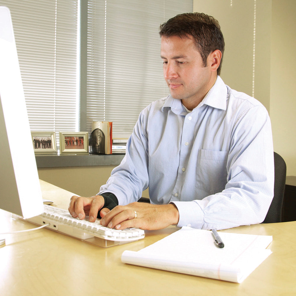 Man sitting at a desk with IMAK Compression Arthritis Thumb using a computer in an office setting.
