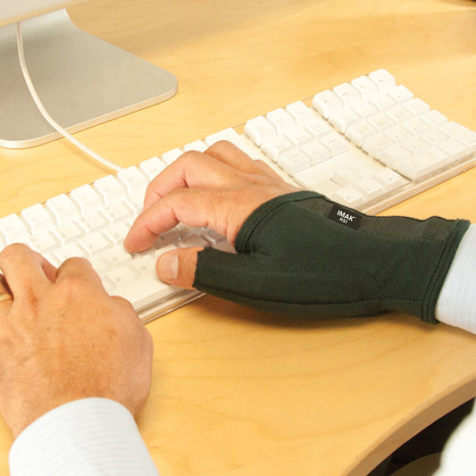 Person using a white keyboard with a IMAK Compression Arthritis Thumb on one hand, sitting at a wooden desk.