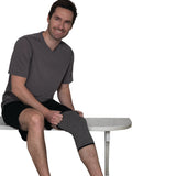 Man sitting on a white bench wearing an IMAK Compression Arthritis Knee Sleeve on his left leg.