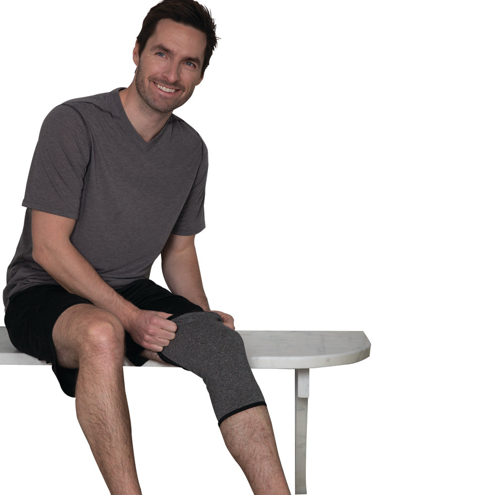 Man sitting on a white bench wearing an IMAK Compression Arthritis Knee Sleeve on his left leg.