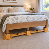 A bed in a styled bedroom with a light beige upholstered frame and bright Tas-Tech Double, Queen King Bed Raisers, shown with white and sage green bedding, pillows, and bedside tables.