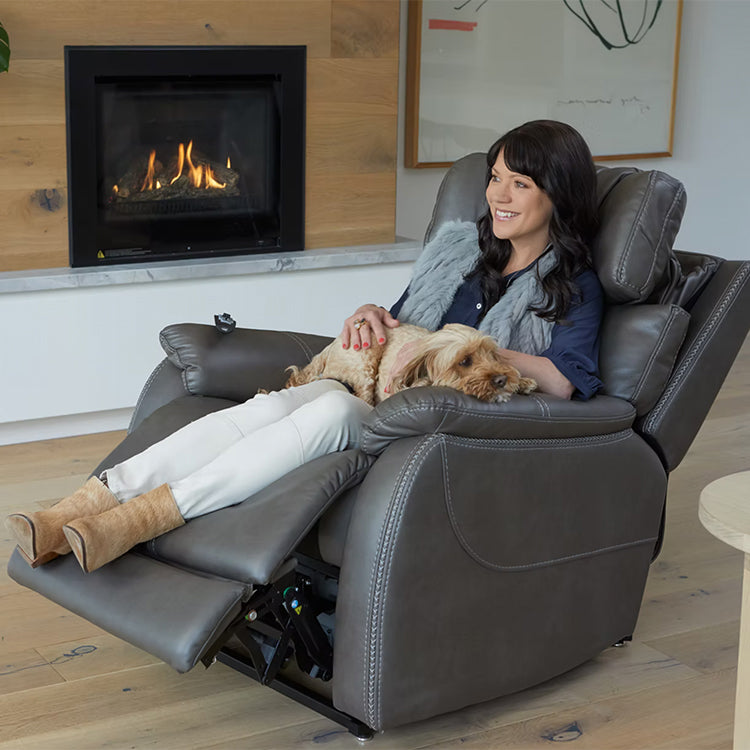 Woman sitting in a Theorem Winslow Power Lift Recliner Chair Smoke with a dog, in front of a fireplace.