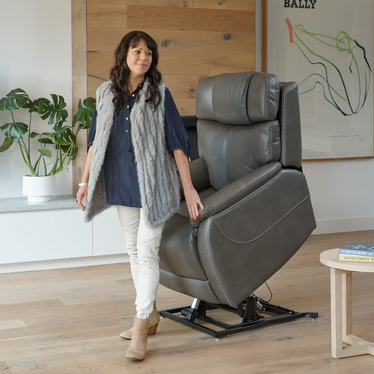 Woman standing next to Smoke Theorem Winslow Power Lift Recliner Chair in a room with wooden flooring and a plant.