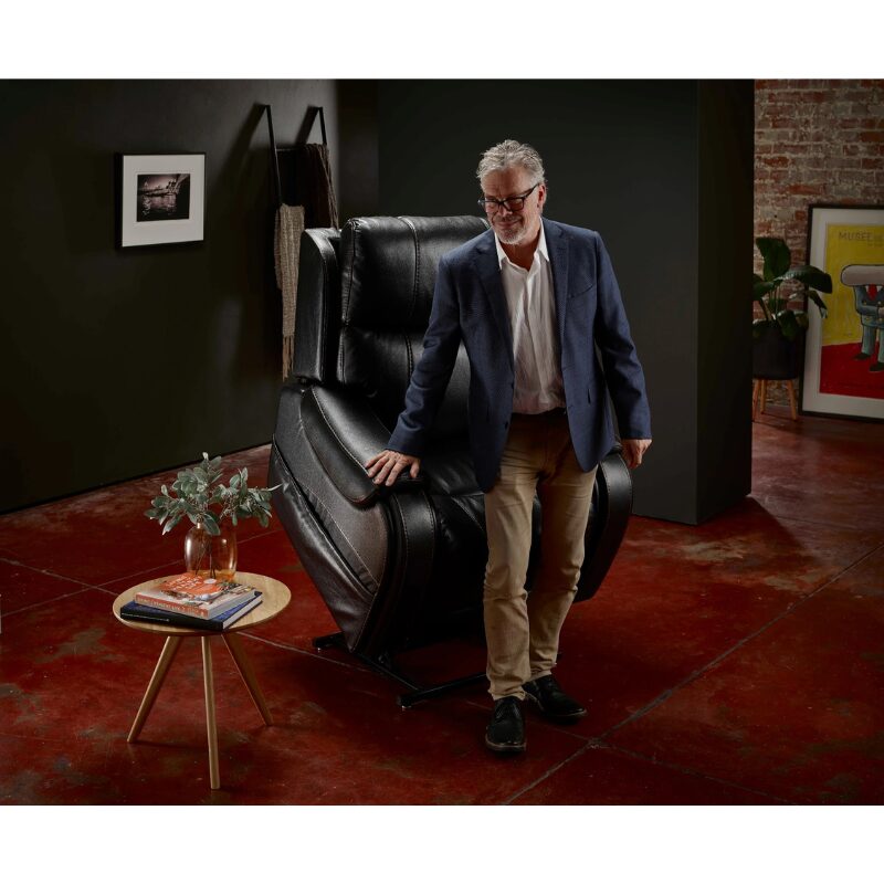 Man standing next to a Theorem Seagrove Power Lift Recliner Chair midnight in a stylish room with a dark wall and red floor.