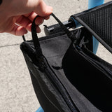 A close-up of a black zippered fabric bag being held open by a hand, with a textured gray concrete ground in the background.