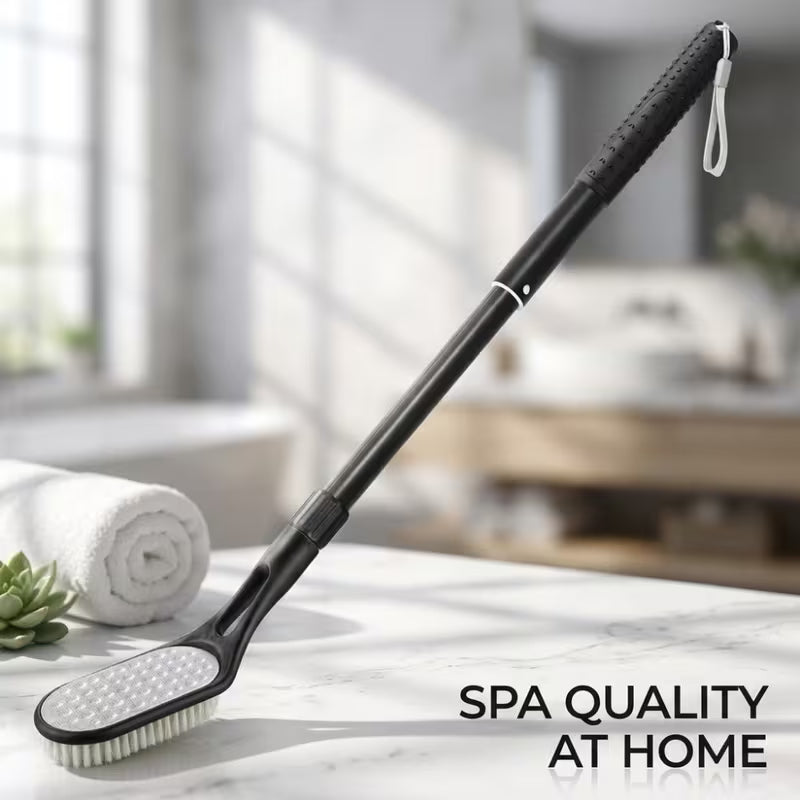 A long-handled black spa cleaning brush with soft bristles, shown resting on a marble countertop in a bright bathroom setting. A rolled towel, small succulent, and soft-focus bathroom background are visible.