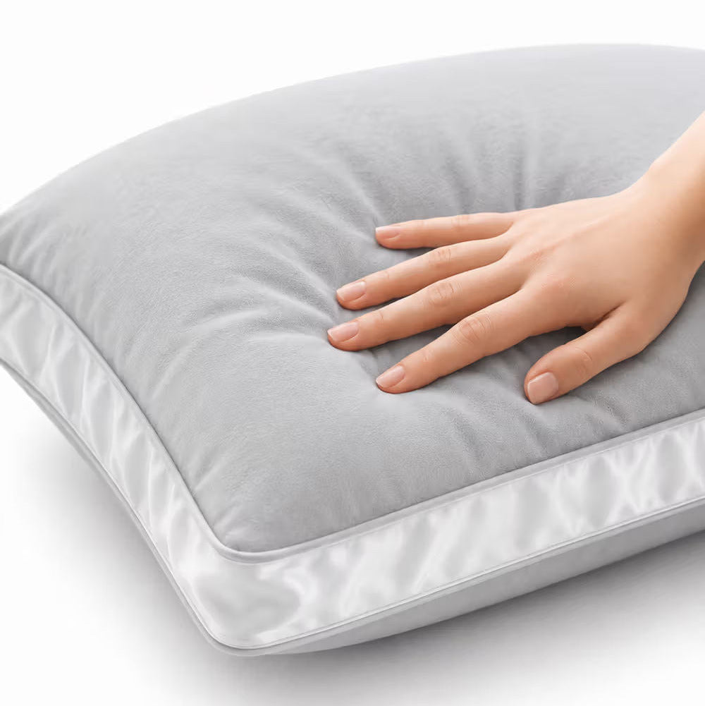 Aicare Conform  pillow with a smooth, plush surface and a satin white border, shown with a hand resting on top against a clean white background.