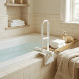 A white Roma Bath Grab Bar mounted over a bathtub in a softly lit bathroom with cream tile, folded white towels, a wooden tray, and bath accessories.