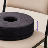 A charcoal icare Supporta Donut Cushion sits on a beige upholstered chair. A purple double-arrow graphic indicates the cushion is adjustable.