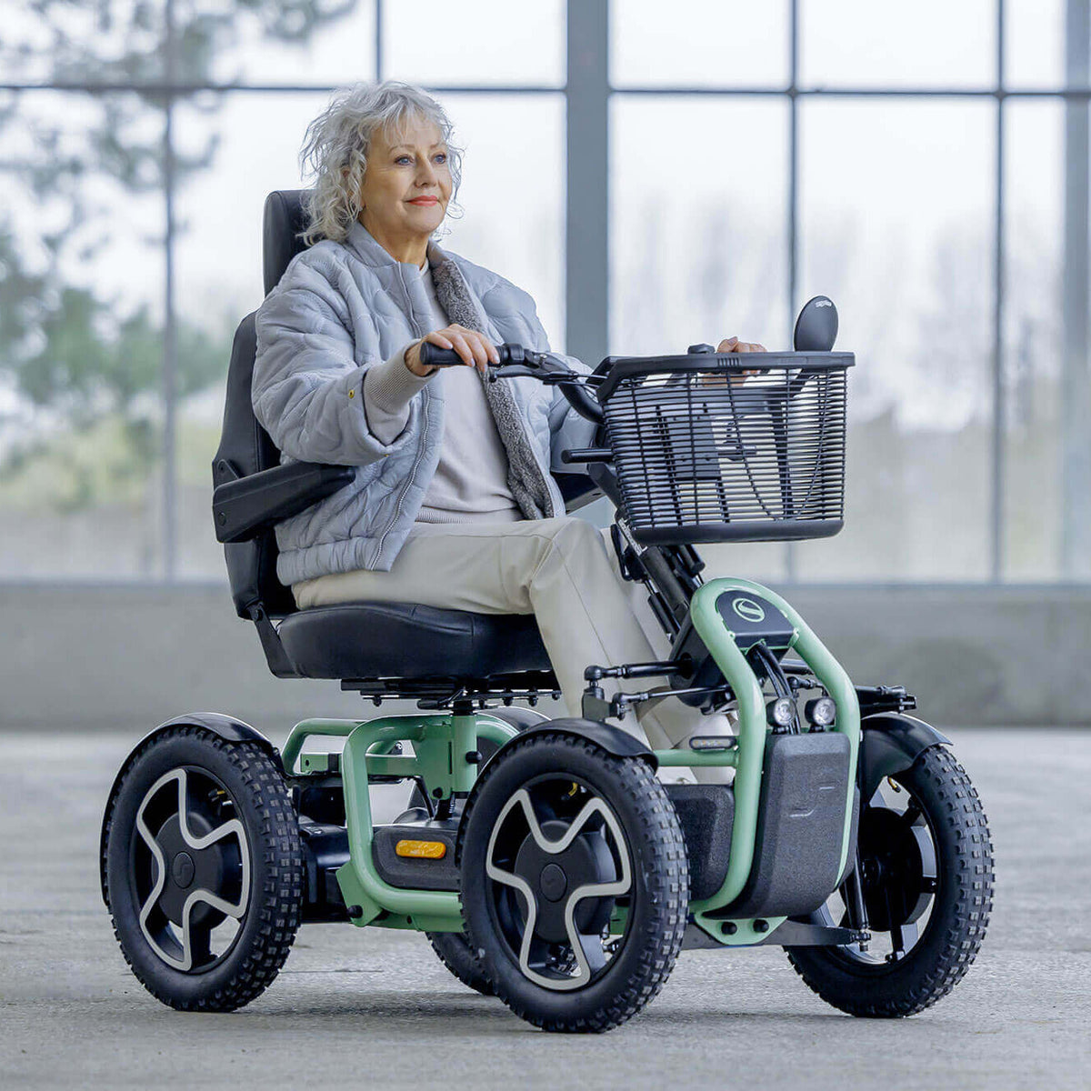 Woman using a STERLING S800 by Scoozy All-Terrain Mobility Scooter in an indoor setting with large windows.