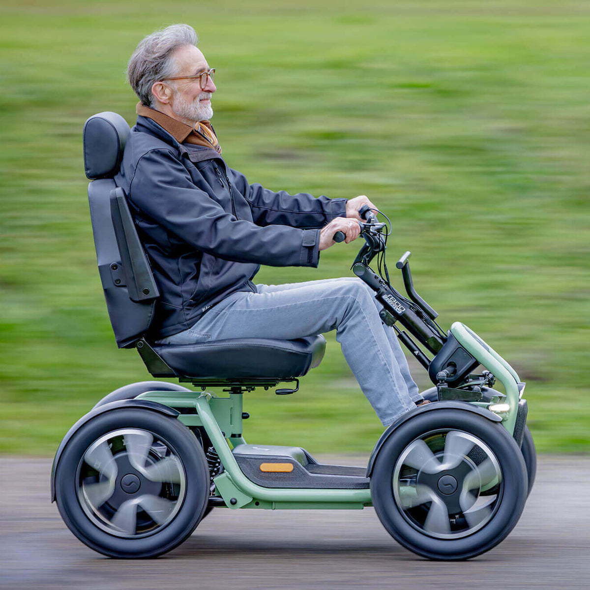 Man using a STERLING S800 by Scoozy All-Terrain Mobility Scooter on a blurred green outdoor background