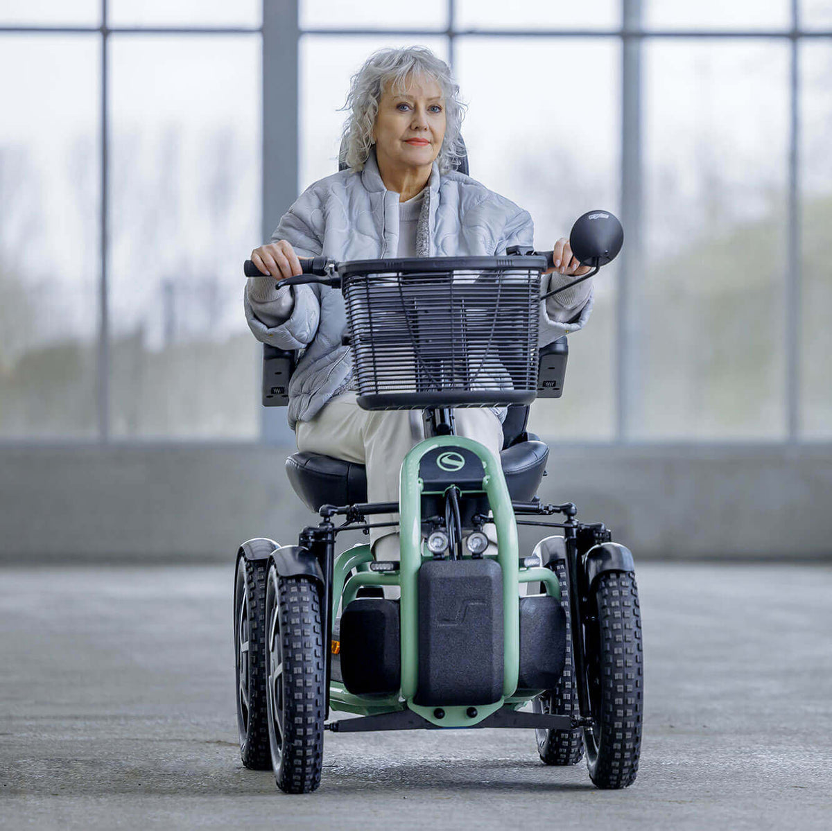 Woman using a STERLING S800 by Scoozy All-Terrain Mobility Scooter in an indoor setting with large windows.