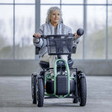 Woman using a STERLING S800 by Scoozy All-Terrain Mobility Scooter in an indoor setting with large windows.