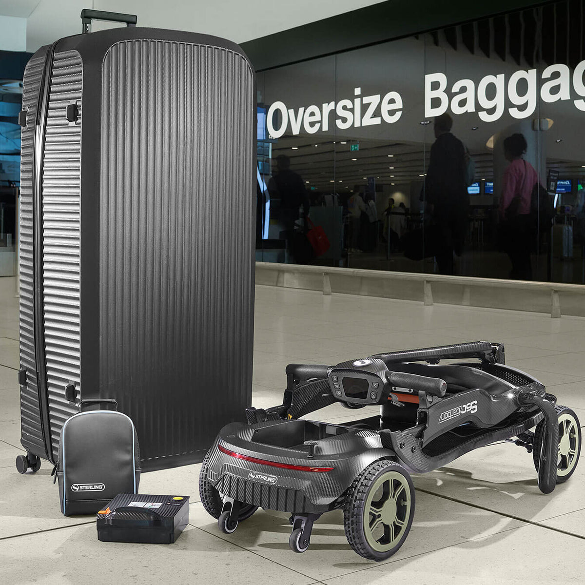 A large black ribbed hard-shell suitcase stands next to a STERLING S50 Carbon Folding Mobility Scooter and matching small bag in an airport terminal. A glass sign in the background reads 'Oversize Baggage'.